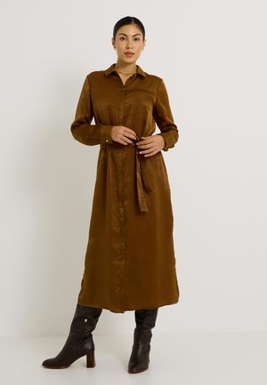 Vestido de camisa de manga larga en bronce, de tejido suave, con botones en la parte delantera, cuello y cintura ajustable, combinado con botas negras de tacón altas hasta la rodilla.