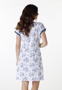 Abito bianco con un motivo floreale blu, maniche corte con bordi blu e un design rilassato fino al ginocchio. Tessuto morbido.