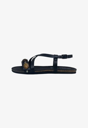 Sandalo piatto nero con sottili cinturini in pelle, fibbia alla caviglia e due borchie decorative rotonde sulla cinghia frontale.