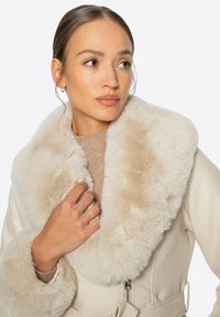 Beżowa skórzana kurtka z sztucznym futrem przy kołnierzu. Kurtka ma paski w talii oraz ribbowe wykończenie na rękawach.