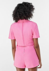 Pink short-sleeve romper in textured fabric, featuring a collar, zipper in the back, and frayed edges for a casual design.