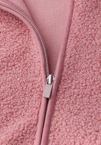 Zbliżenie na częściowo zapiętą różową polarową kurtkę z metalowym suwakiem i teksturowaną, kręconą powierzchnią materiału.