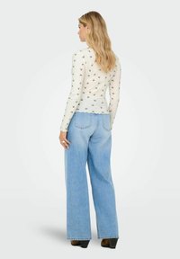 Hvid langærmet top med lille blomstermønster, parret med løse blå denim breddebenede jeans. Sweateren har bølget kant og ribbegarn.