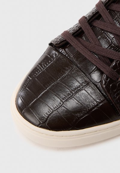Καφέ δερμάτινο αθλητικό παπούτσι με ανάγλυφη υφή κροκόδειλου, στρογγυλή μύτη και αντίθετη λευκή λαστιχένια σόλα· διαθέτει σκούρα καφέ κορδόνια.