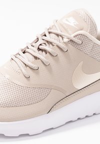 Béžová teniska Nike Air Max Thea s síťovaným svrškem, hladkými detaily, plochými tkaničkami a bílou podrážkou s jemným logem.