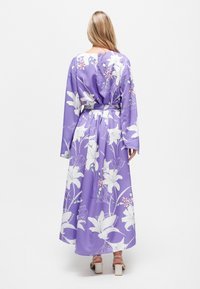Langes, lila Blumenkleid mit weißen Lilienmustern, leichtem Stoff, langen Ärmeln und gebundenem Taillengurt, mit einem fließenden Rock.