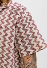 Camicia a maniche corte con un motivo a zigzag rosso e bianco, realizzata in un tessuto leggero e testurizzato, con colletto e vestibilità ampia.