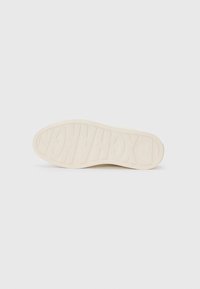 Zool van een schoen, getextureerd rubber in crème kleur, met "EXCHANGE" in dikke letters op het oppervlak geperst. Rond neusontwerp, platte profiel.