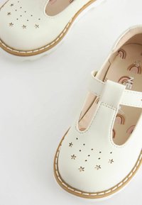 Vita läderskor med stjärnformade utskärningar, T-rem-design och beige sula. Insidan har ett färgglatt regnbågsmönster.