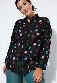 Svart skjorta med knappar som har färgglada juvelmönster i rosa, blått och grönt. Långa ärmar med en avslappnad passform. Texturerad tyg.