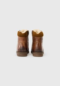 Barna bőr bokacsizma puha, krém színű béléssel, velúr felső résszel és érdes gumitalppal. Hátsó nézet, melyen a cipzáras záródás látható.