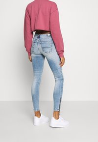 Jeans ajustados, de un azul claro desgastado, con cinco bolsillos y detalles metálicos en los tobillos, combinados con un sudadera corta rosa y zapatillas blancas.