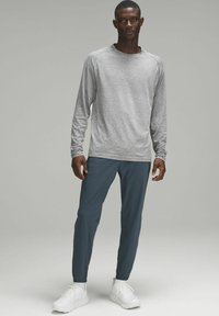 Grå långärmad skjorta med rund halsringning, kombinerad med teal joggerbyxor och vita sportskor. Slät textur och figursydd passform.