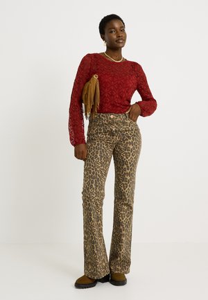 Top de manga larga de patrón rojo combinado con pantalones acampanados de leopardo marrón y botas de tobillo marrones. Acentuado con un bolso marrón con flecos.