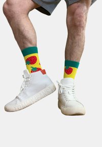 Zapatillas altas blancas con suelas texturizadas, con la marca "TOMMY JEANS". Combinadas con calcetines amarillos brillantes adornados con fresas rojas.