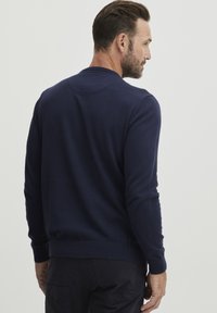 Temno modra pulover s okroglim izrezom, rebrastimi manšetami in robom. Narejen iz mehkega blaga, ki se ponaša z gladko teksturo in minimalističnim dizajnom.