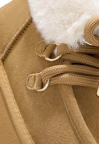 Botín de tobillo de ante color marrón con un suave cuello de piel sintética blanca, cordones trenzados y ojales metálicos para un ajuste seguro.
