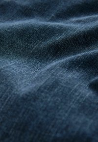 Mörkblå denimtyg med en mjuk textur, som har en subtil glans och synligt vävmönster, som visar försiktiga veck och skrynklor.