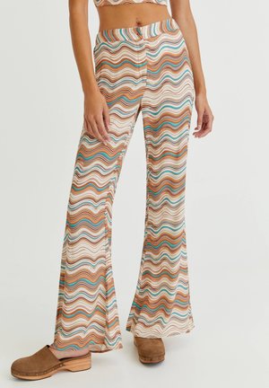 Los pantalones acampanados en tejido tejido presentan una base crema con coloridas rayas onduladas en marrón, naranja y azul verdoso. El diseño incluye una cintura ajustada.