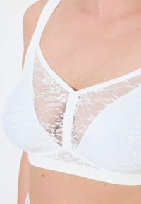 Witte kanten bralette met een delicaat bloemenpatroon, voorzien van doorzichtige panelen aan de bovenkant en een stevige band eronder voor ondersteuning.