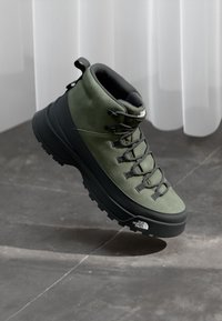 Green suede hiking boot with black rubber sole, padded collar, and reinforced eyelets, featuring a textured design and lace-up closure.