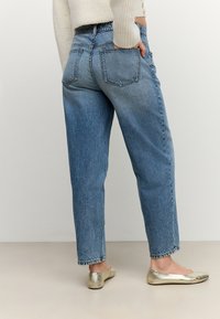 Világoskék farmernadrág laza szabással, magas derékkal és ötpocketes kialakítással, fémes arany balerinacipővel párosítva. Texturált anyag, amelynél a szín elhalványult.