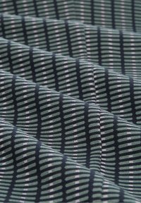 Gros plan d'un tissu plié présentant un motif répétitif de tirets horizontaux noirs et verts formant des rayures verticales.