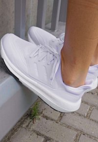 Witte sportschoenen met een bovenwerk van mesh, geïntegreerde veters en gevoerde zolen. Zachte textuur met subtiele ontwerpelementen en een zwarte buitenzool.