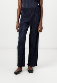 Pantalons larges plissés navy en tissu lisse et léger avec une coupe décontractée. Présente des rayures verticales subtiles et une taille élastique.
