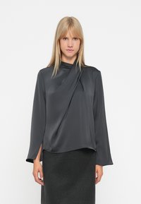 Blusa grigio scuro a maniche lunghe con scollatura drappeggiata. Realizzata in tessuto liscio con leggero lucido. Presenta spacchi laterali all'orlo.