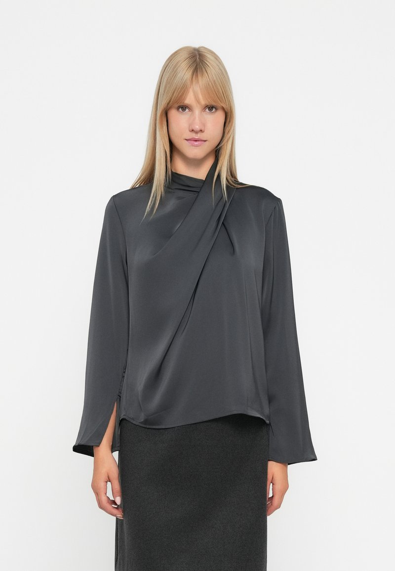 Blusa grigio scuro a maniche lunghe con scollatura drappeggiata. Realizzata in tessuto liscio con leggero lucido. Presenta spacchi laterali all'orlo.