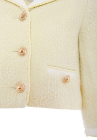 Giacca in tweed color crema con finitura testurizzata, caratterizzata da bottoni dorati e una piccola tasca con dettaglio decorativo del bottone.