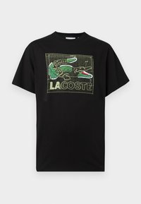 Μαύρο βαμβακερό T-shirt με μοτίβο πλέγμα, γραφικό πράσινου κροκοδείλου και κείμενο "LA COSTE" σε έντονες γραμματοσειρές σε όλη την επιφάνεια. Άνετη εφαρμογή.