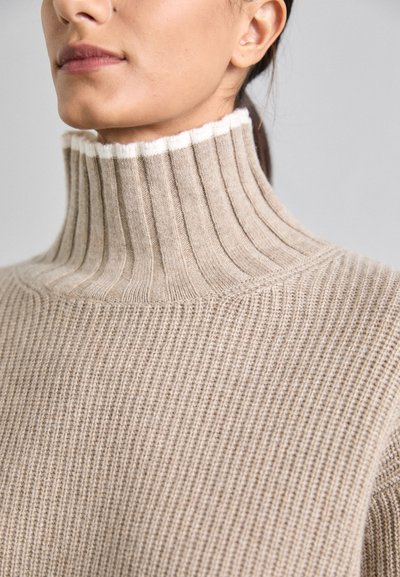Beige Rippstrickpullover mit hohem, strukturiertem Kragen, der an der Kante einen weißen Akzent hat. Weicher, warmer Stoff mit lockerer Passform.
