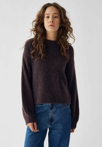 Pulover tricotat de culoare mov închis, cu mâneci lungi, guler rotund și o croială lejeră, asortat cu blugi de denim albastri, cu talie înaltă.
