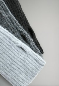 Trzy kawałki dzianiny w odcieniach czerni, szarości i jasnej szarości, prezentujące teksturowany wzór o różnej grubości.