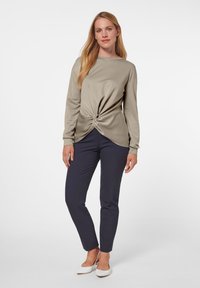 Beige Langarm-Oberteil mit verdrehtem Vorderteil, kombiniert mit navyblauen Slim-Fit-Hosen und weißen Slippern. Glatter Stoff mit leichtem Glanz.