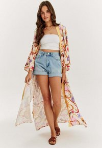 Dlouhý, lehký kimono z jemného materiálu s barevným květinovým vzorem. Nosené přes bílé crop top a džínové šortky, s hnědými sandály.