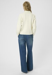 Crèmekleurige gebreide trui met een kraag, gecombineerd met wijde blauwe denim jeans. De jeans hebben subtiele vervaging en details op de achterzakken.
