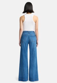 Helle Bluejeans mit weitem Bein, hohem Bund und vier Taschen. Das Material ist weich mit einer glatten Textur und auffälligen Nahtdetails.