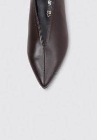 Zapato de cuero marrón con punta afilada y textura suave, que presenta un diseño central en forma de V y costuras mínimas en la parte superior.