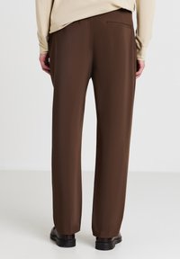 Braune maßgeschneiderte Hosen mit geradem Schnitt, glatter Textur und einer einzelnen Gesäßtasche. Merkmale sind ein minimalistisches Design und ein leichtes Schimmern.