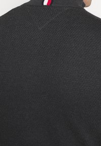 Maglione lavorato a maglia nero con colletto alto, caratterizzato da un accento a strisce rosse, bianche e blu attorno al collo. Tessuto testurizzato con un motivo discreto.