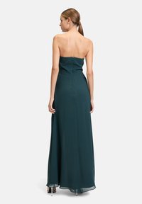 Langes, trägerloses Abendkleid aus dunkelgrünem Stoff. Enganliegendes Oberteil mit Reißverschluss auf der Rückseite und einem fließenden Rock. Glatte Textur.
