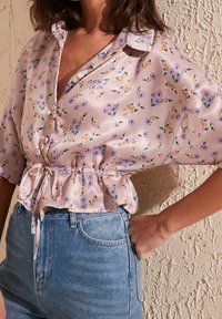 Blusa in satin rosa chiaro con motivo floreale, maniche corte, colletto e vita sfiancata, abbinata a pantaloni shorts di jeans a vita alta.