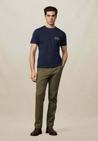 Camiseta azul marino con diseño de bolsillo en el pecho, combinada con pantalones verde oliva y botas de tobillo marrones. Tela suave, ajuste entallado.