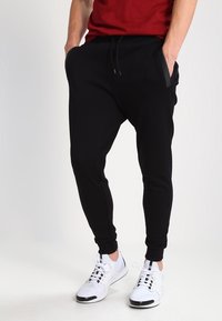 Czarne spodnie dresowe o luźnym kroju, z elastycznym pasem i dwoma bocznymi kieszeniami, zestawione z białymi sportowymi butami. Gładka faktura materiału.