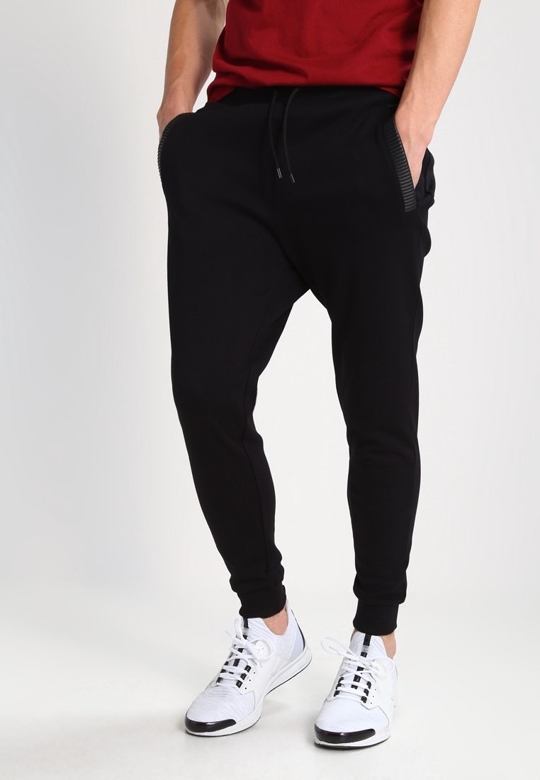 Czarne spodnie dresowe o luźnym kroju, z elastycznym pasem i dwoma bocznymi kieszeniami, zestawione z białymi sportowymi butami. Gładka faktura materiału.