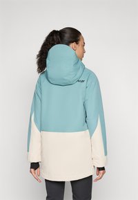 Turquoise and cream color-blocked jacket with a hood, featuring a logo on the back, smooth fabric, and adjustable cuffs.