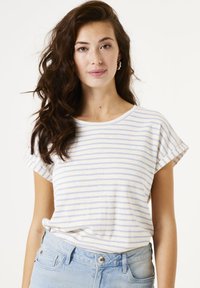 Camiseta a rayas en crema claro y azul, con cuello redondo y mangas cortas enrolladas. Combinada con unos pantalones vaqueros de talle alto en azul claro.